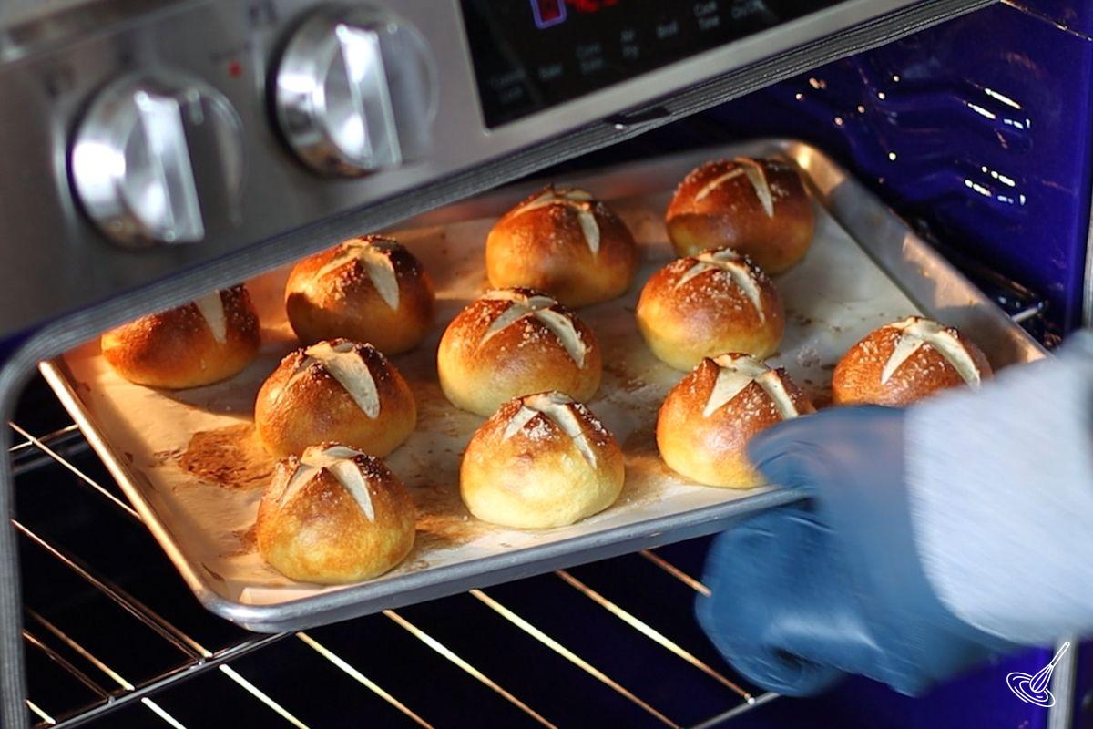 Someone taking a tray of pretzel slider buns out of the oven.