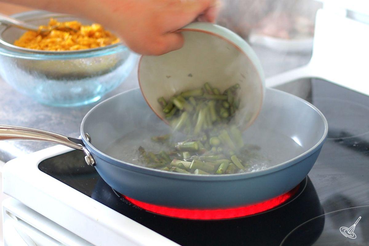 Someone adding pieces of asparagus to a pan of simmering water.