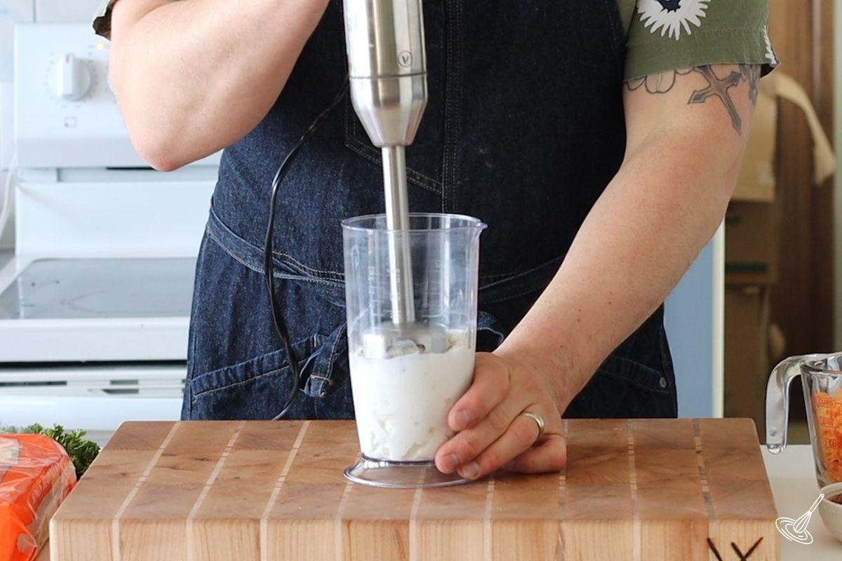Someone using a stick blender to blend cottage cheese.