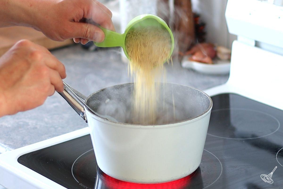 Someone adding orzo to a pot of simmering water.