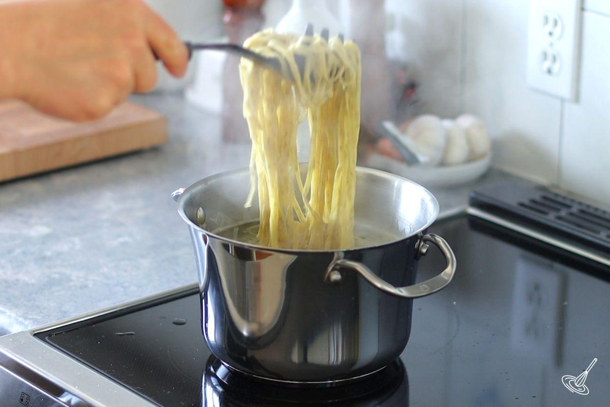 Someone taking cooked pasta out of a pot of boiling water.