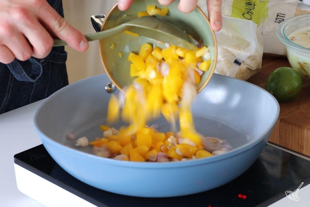 Someone adding a bowl of choped vegetables to a large skillet. 