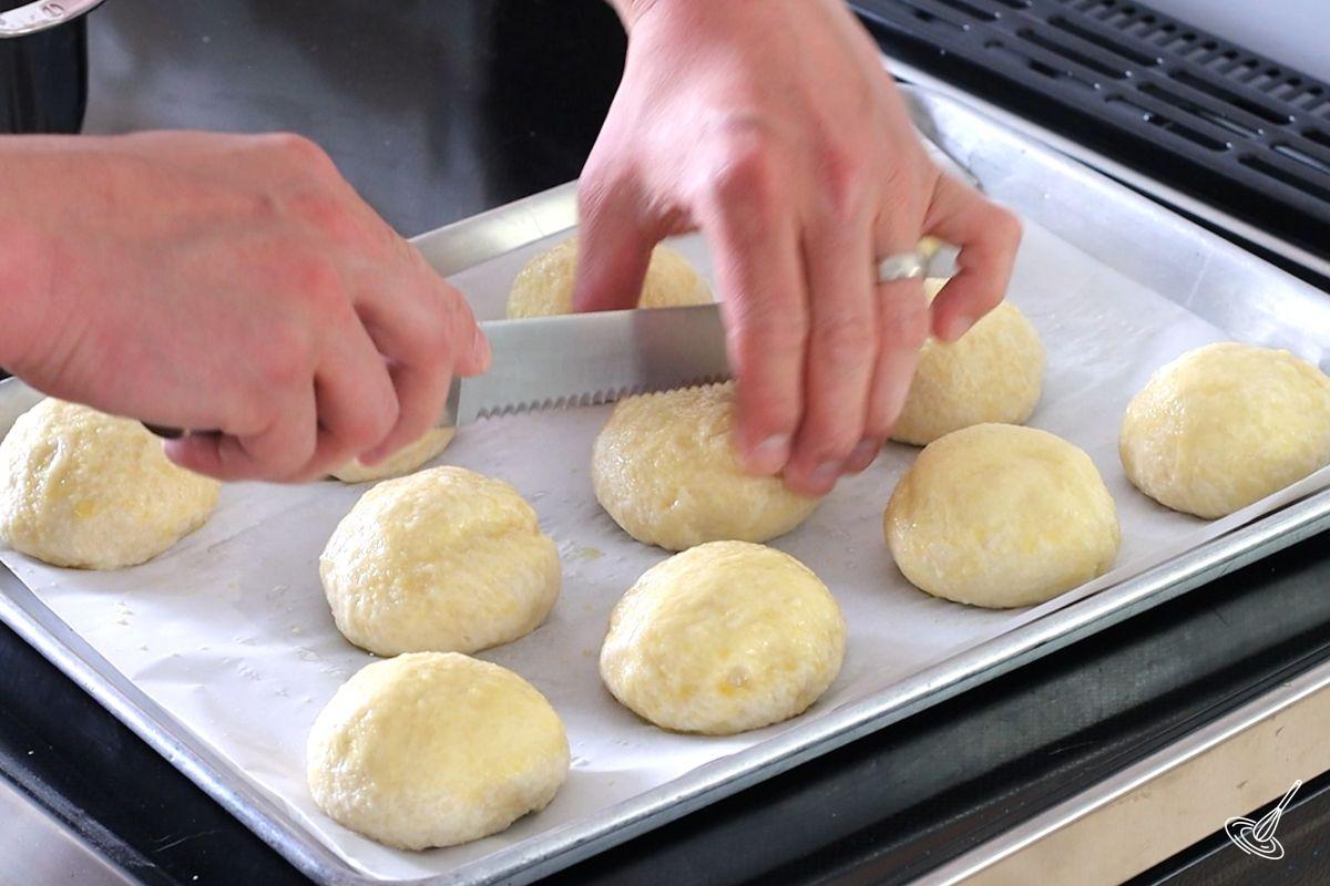 Someone cutting lined on the top of pretzel buns. 
