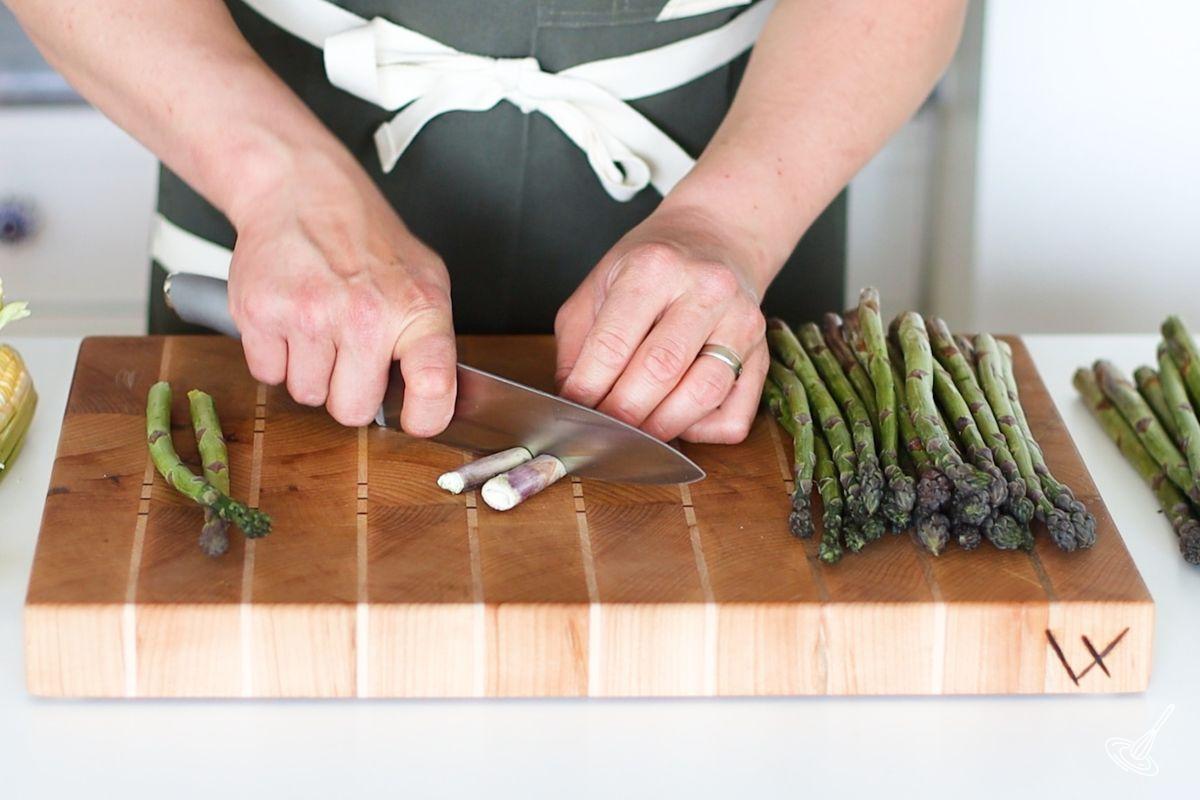 Someone using a knife to cut the tips off of asparagus.