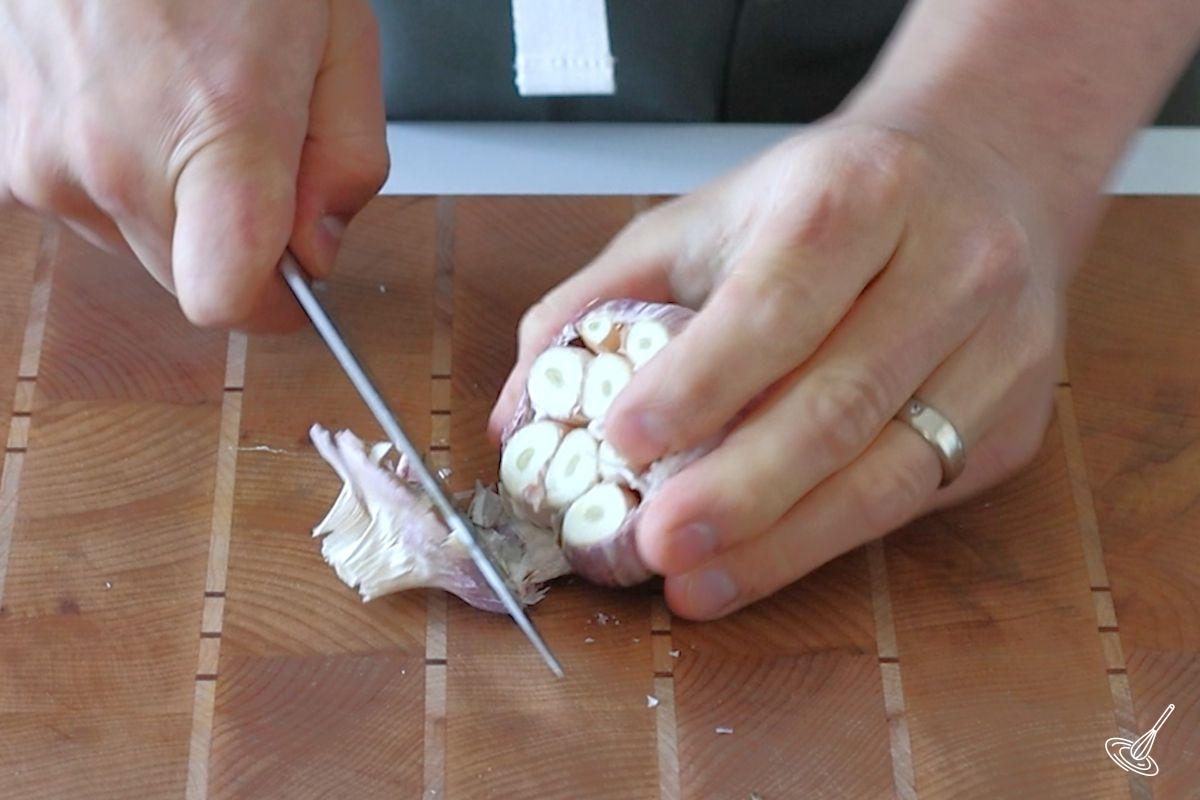 Someone cutting the top off of a garlic bulb.