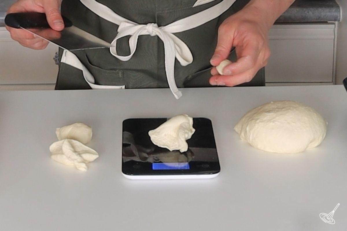 Someone weighing a piece of pretzel dough on a food scale.