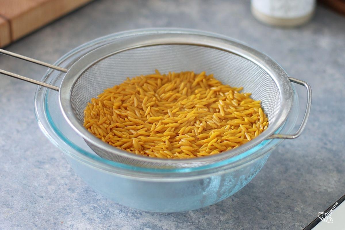 Cooked orzo in a fine mesh strainer over a glass bowl.