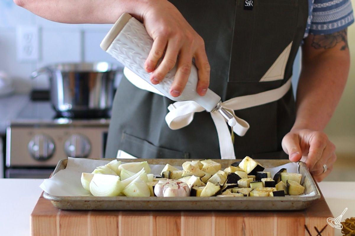 Someone drizzling olive oil on a tray of cubed vegetables.