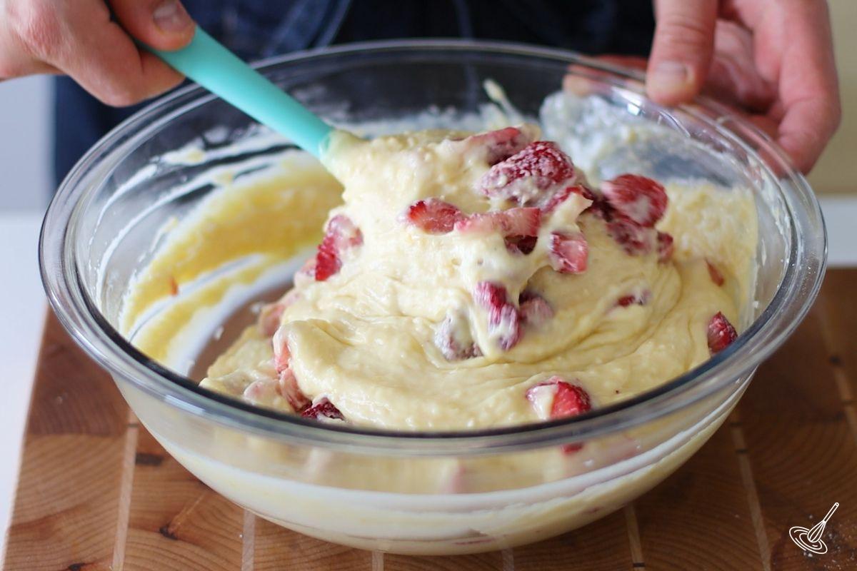 Someone folding strawberries in a bowl of cake batter.