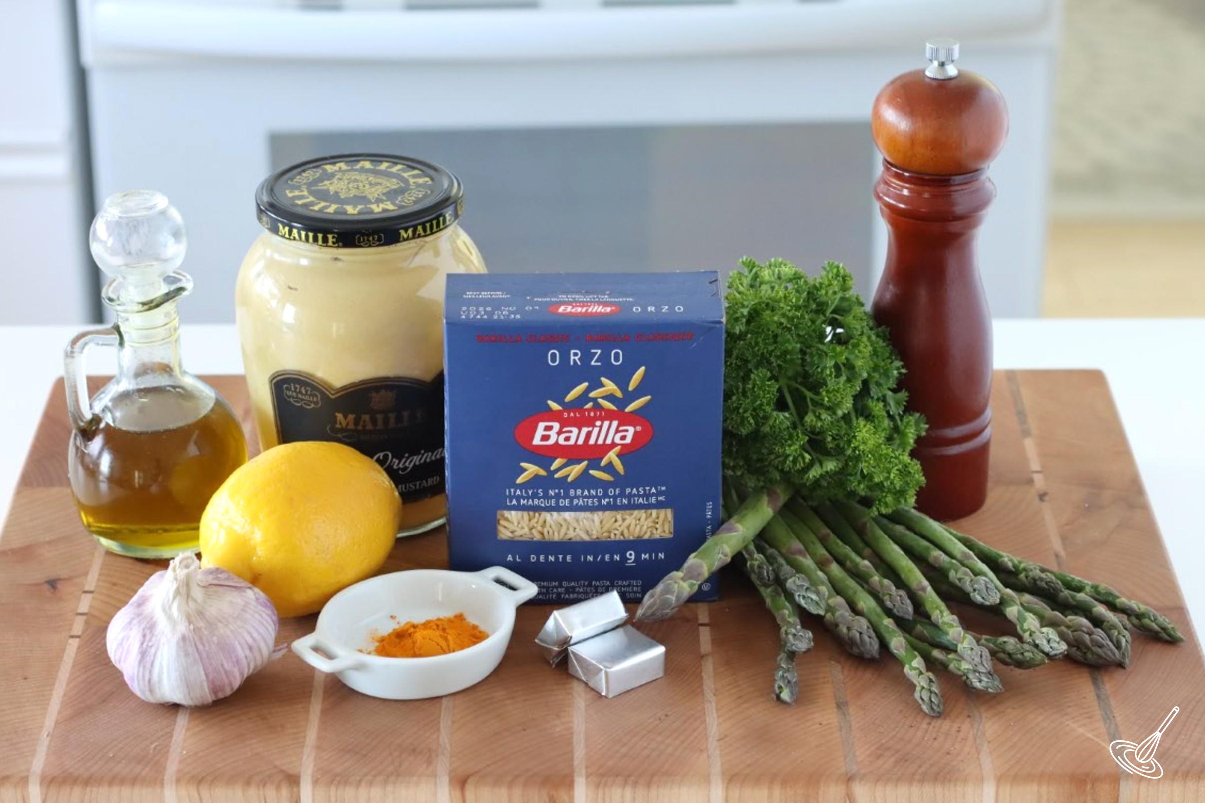 Ingredients on a cutting board, including asparagus, lemon, garlic, and orzo.