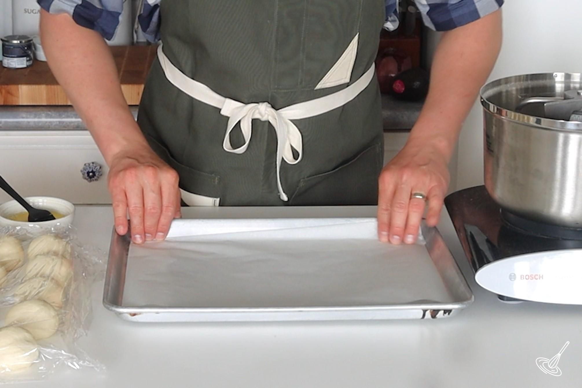 Someone lining a baking tray with parchment paper.