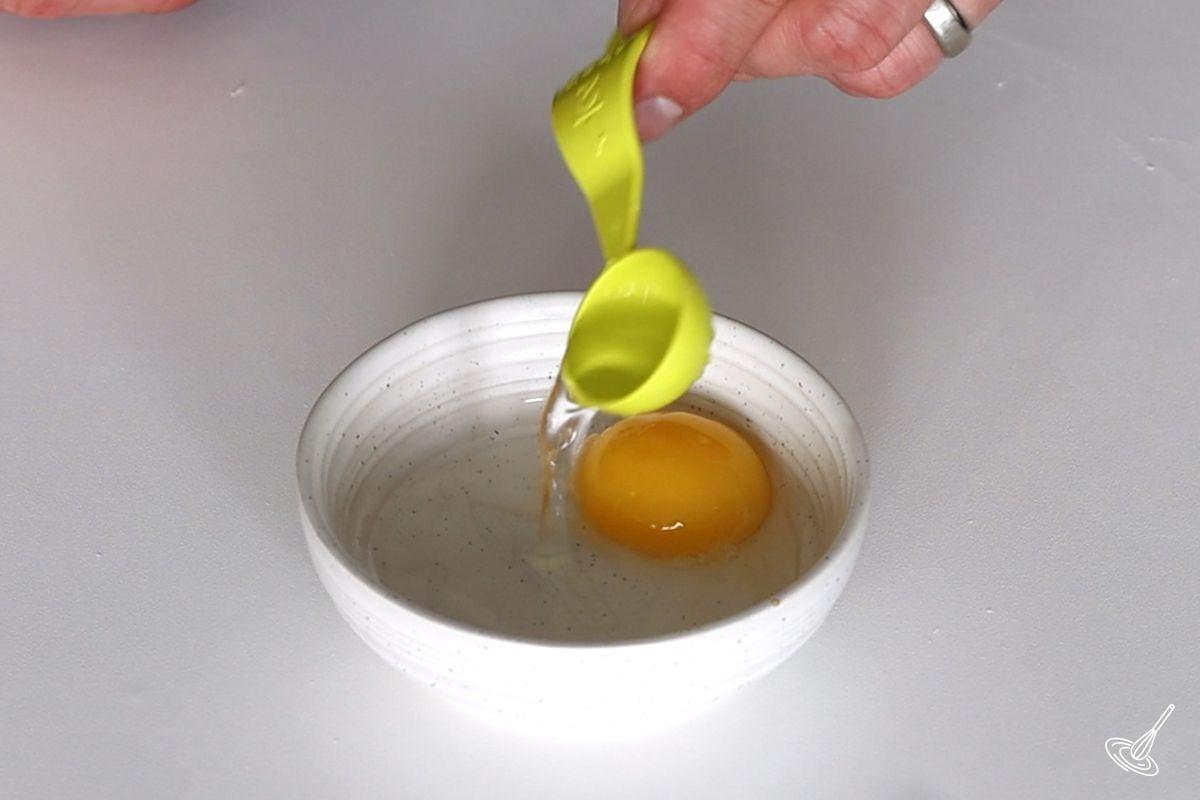 Someone adding water to an egg yolk in a bowl.