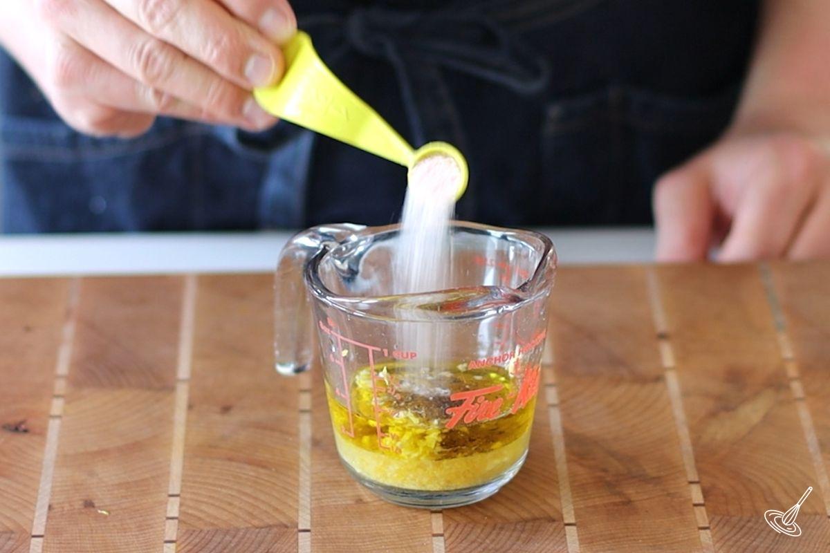 Someone adding salt to a measuring cup of lemon dressing.