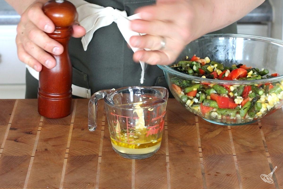 Someone adding salt to a measuring cup of salad dressing. 