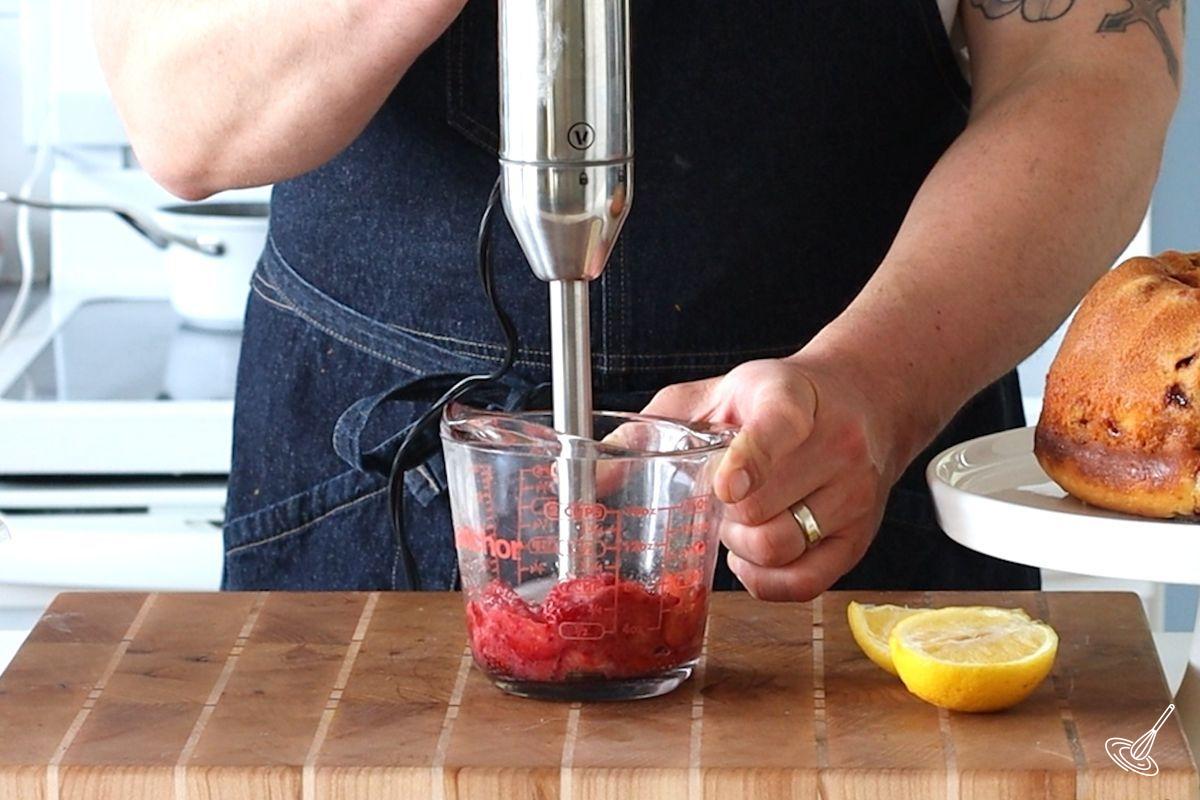 Someone using a stick blender to puree strawberries.