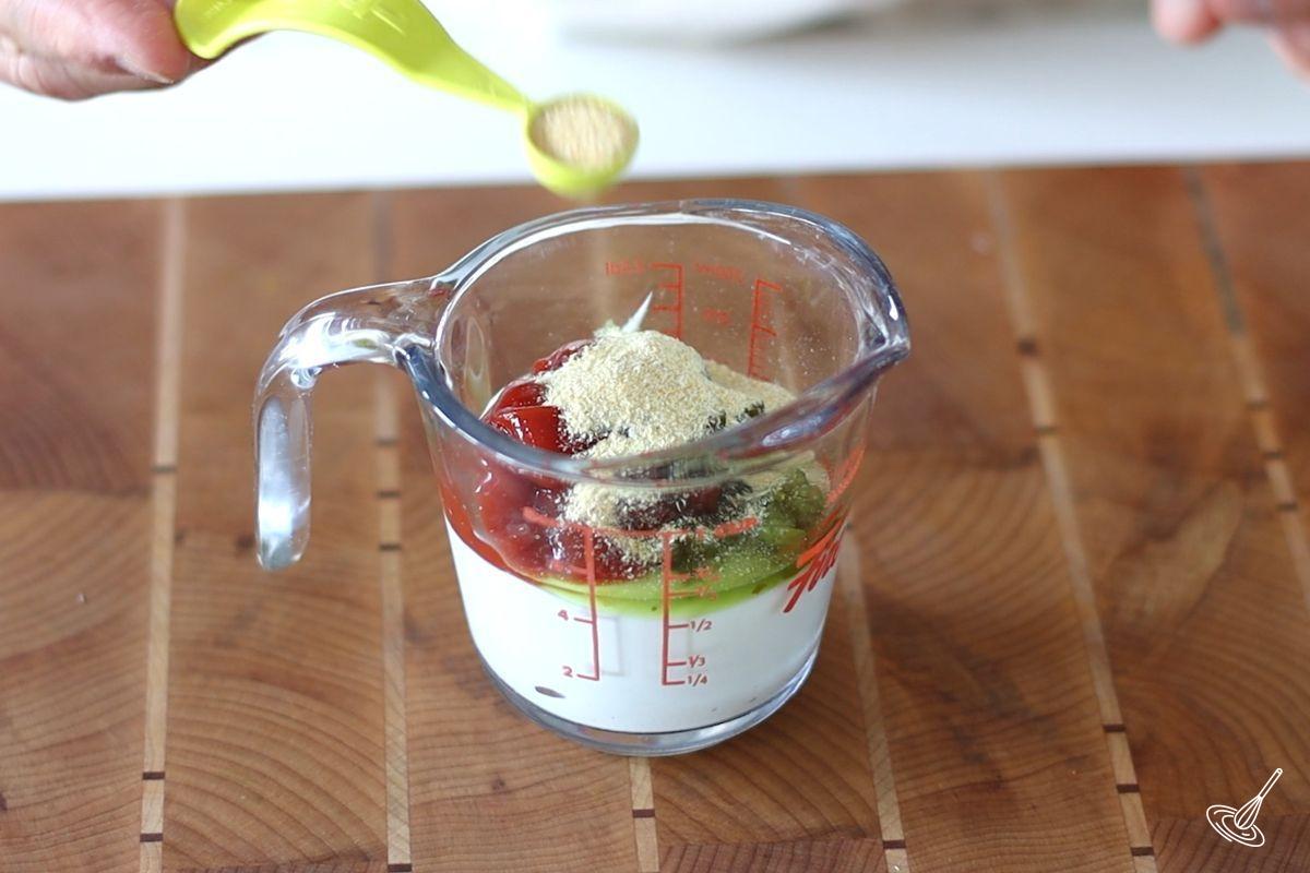 Someone adding garlic powder to a measuring cup to make Thousand Island Dressing. 