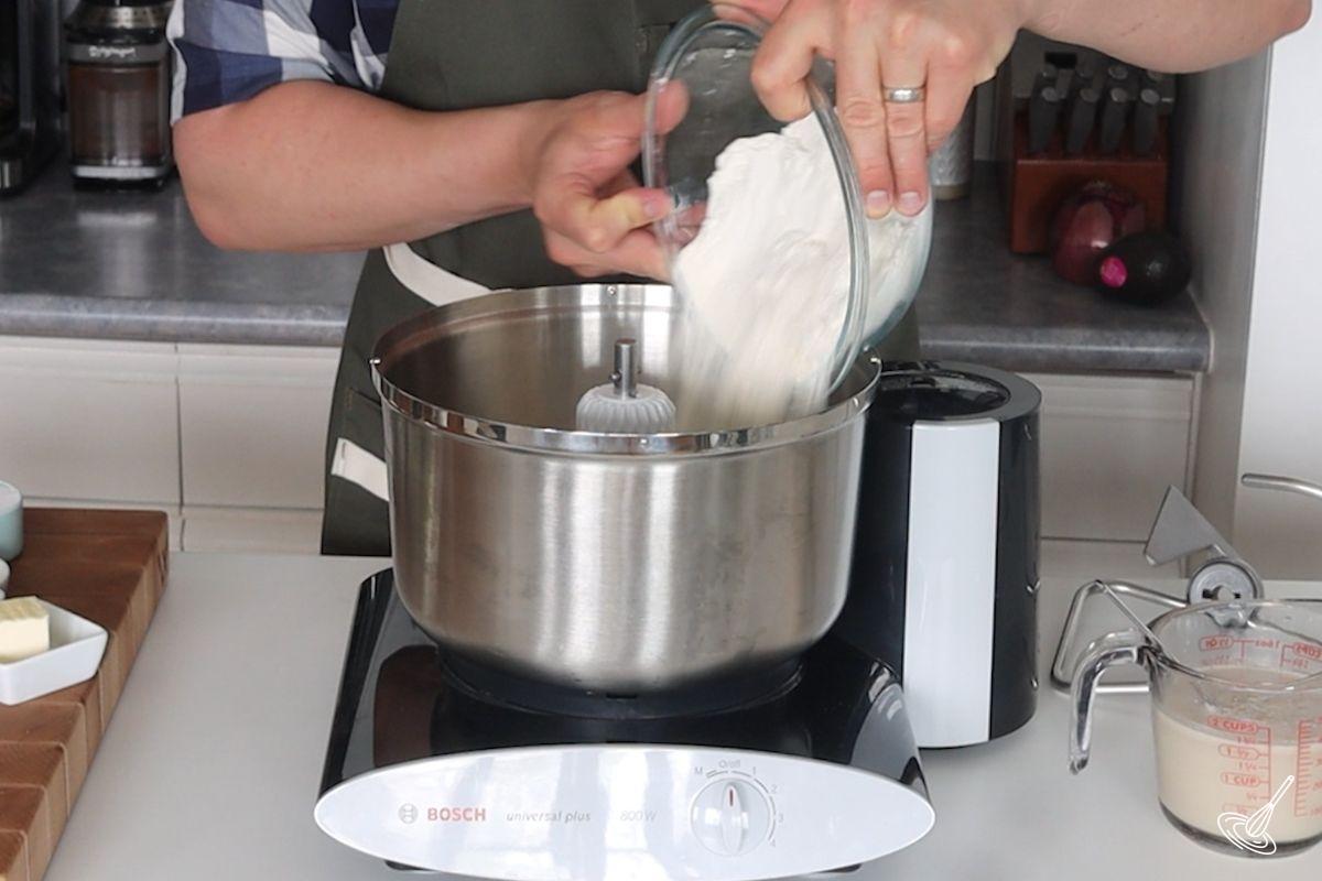 Someone adding flour to a stand mixer.