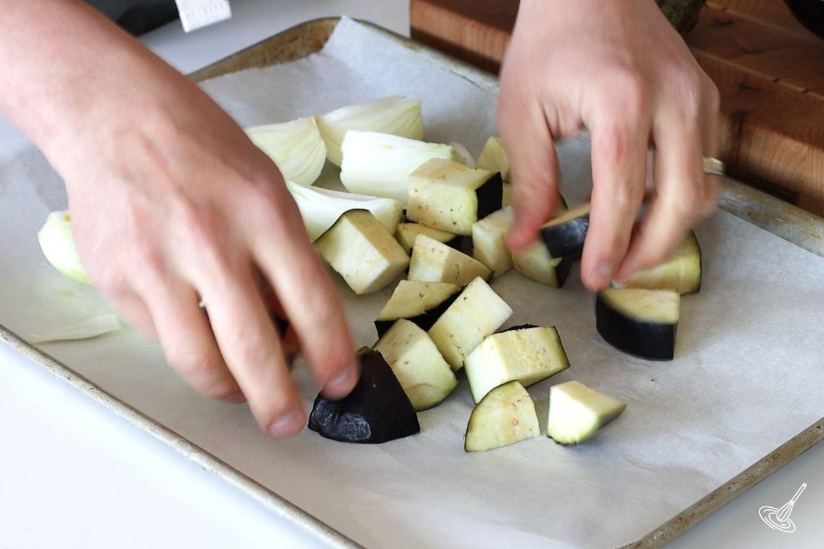Someone placing cubes of aubergine on a baking tray. 