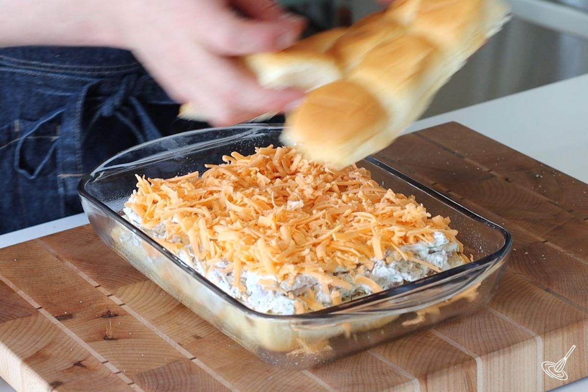 Someone placing the top part of the buns over the crack chicken sliders.