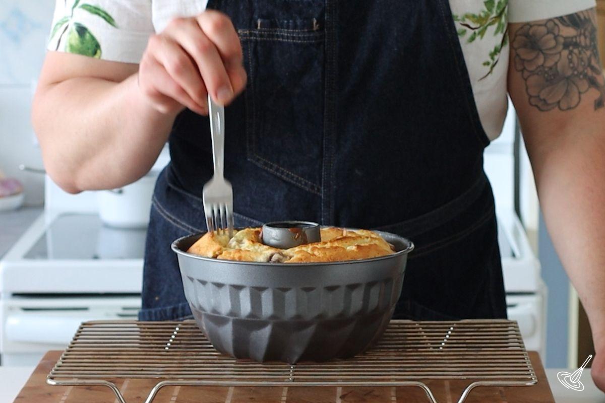Someone using a fork to poke holes on top of a baked Strawberry Lemonade Bundt Cake.