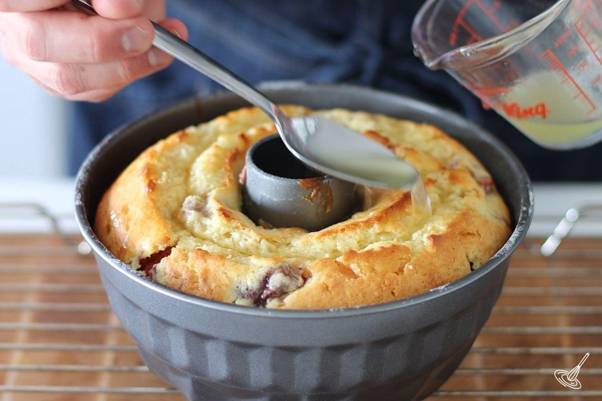 Someone pouring lemon syrup on top of a baked Strawberry Lemonade Bundt Cake