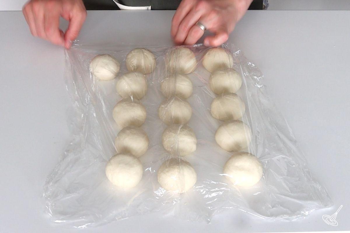 Someone covering pretzel dough balls with plastic wrap.