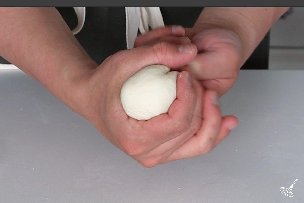 Someone shaping a piece of dough into a ball.
