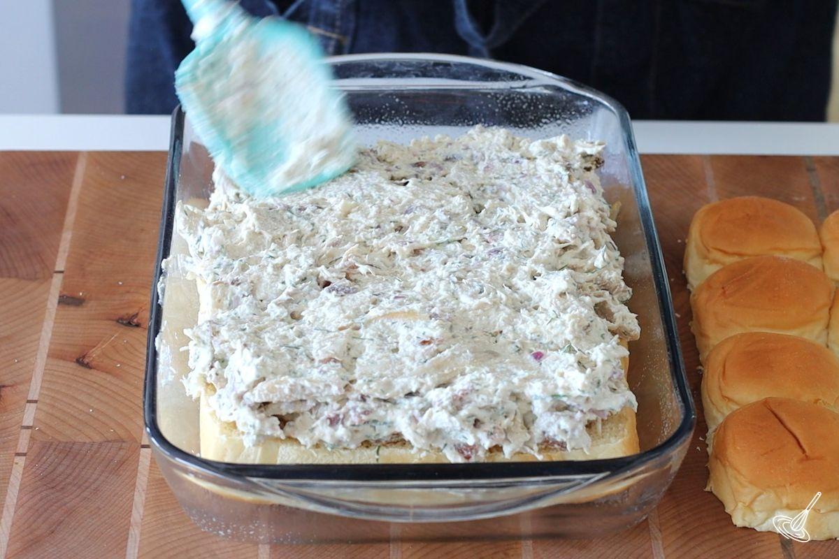 Someone spreading the crack chicken mixture over the bottom part of the buns. 