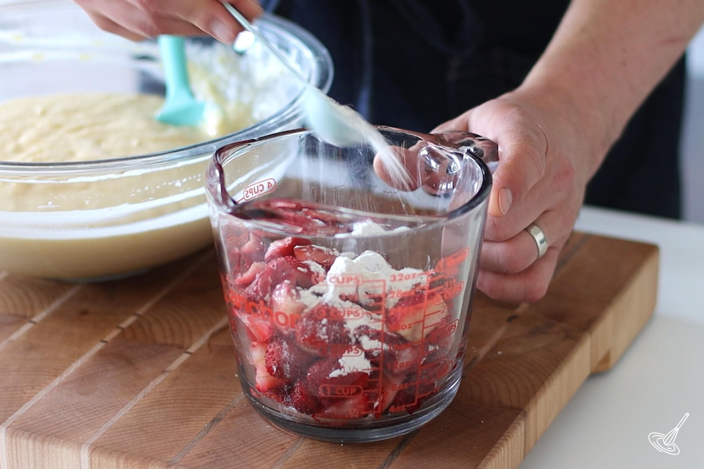 Someone sprinkling flour over chopped strawberries.