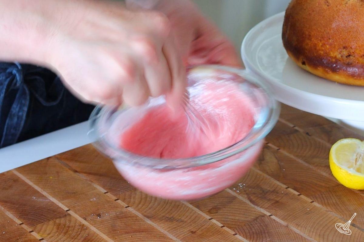 Someone whisking a bowl of strawberry icing. 