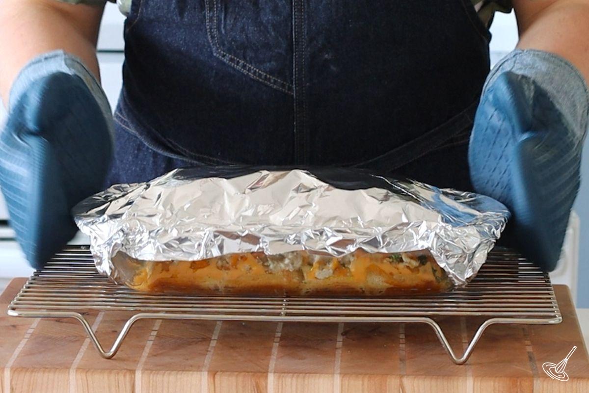 A baking dish covered with aluminum foil, on a cooling rack.