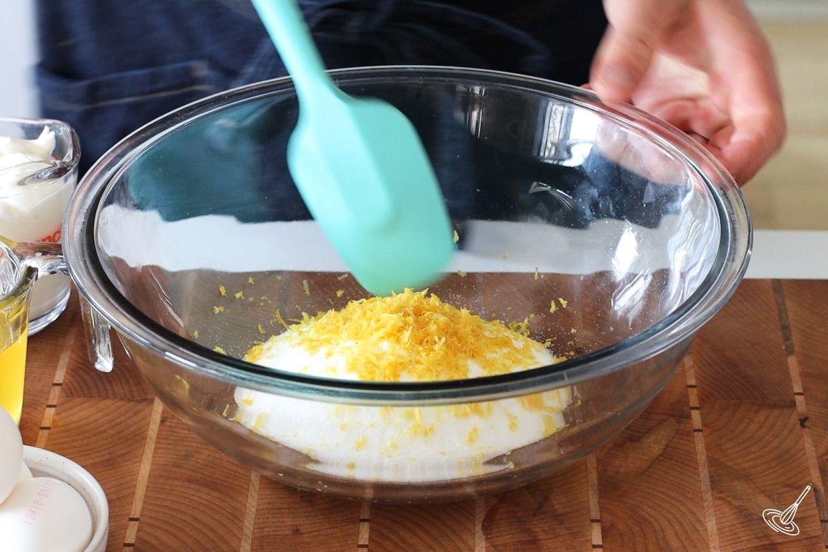 Someone mixing lemon zest and sugar in a large bowl.