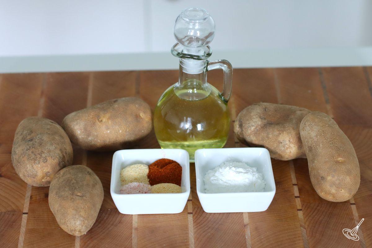 Ingredients on a cutting board including potatoes, a container of cooking oil, cornstarch, and spices.