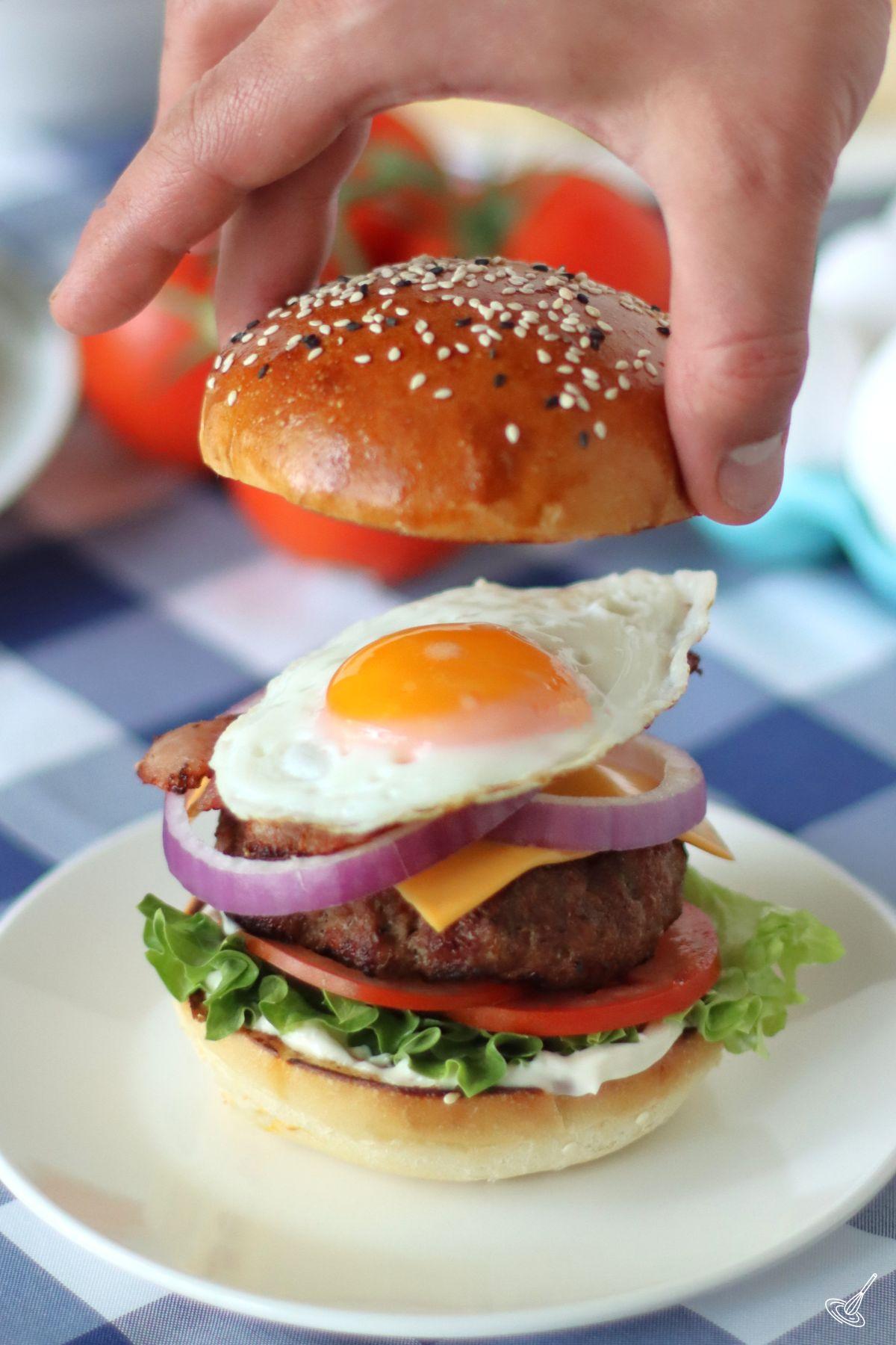 Someone placing the top bun on a Bacon Egg Cheese Burger. 