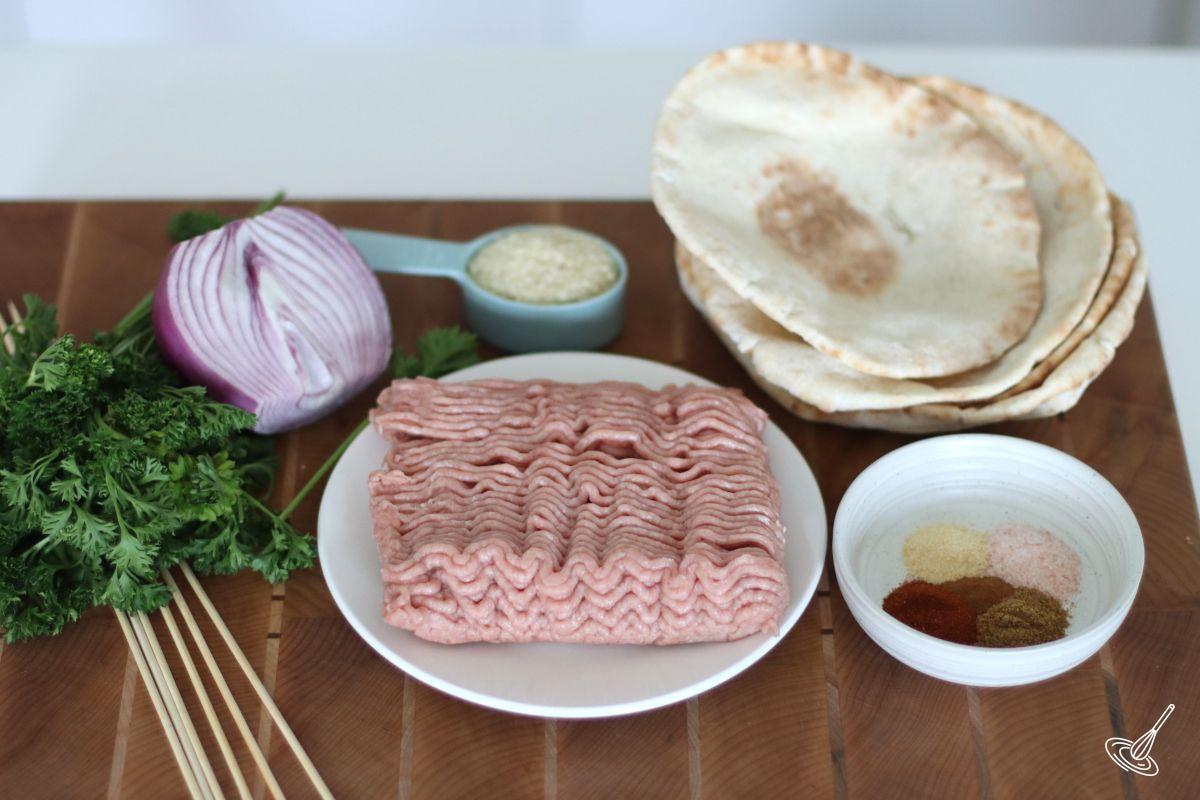 Ingredients on a cutting board, including ground turkey, onion, parsley, spices, and pita bread.