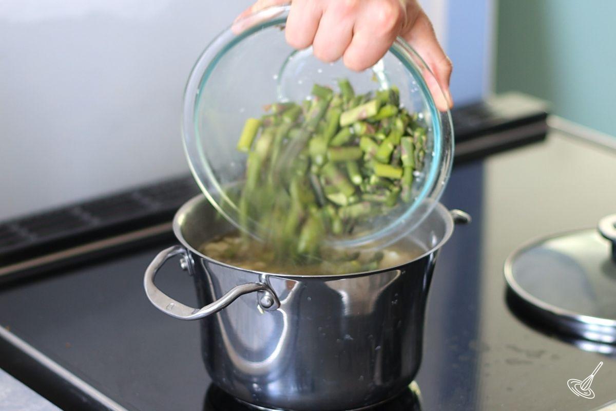 Someone adding chopped asparagus to a soup pot. 