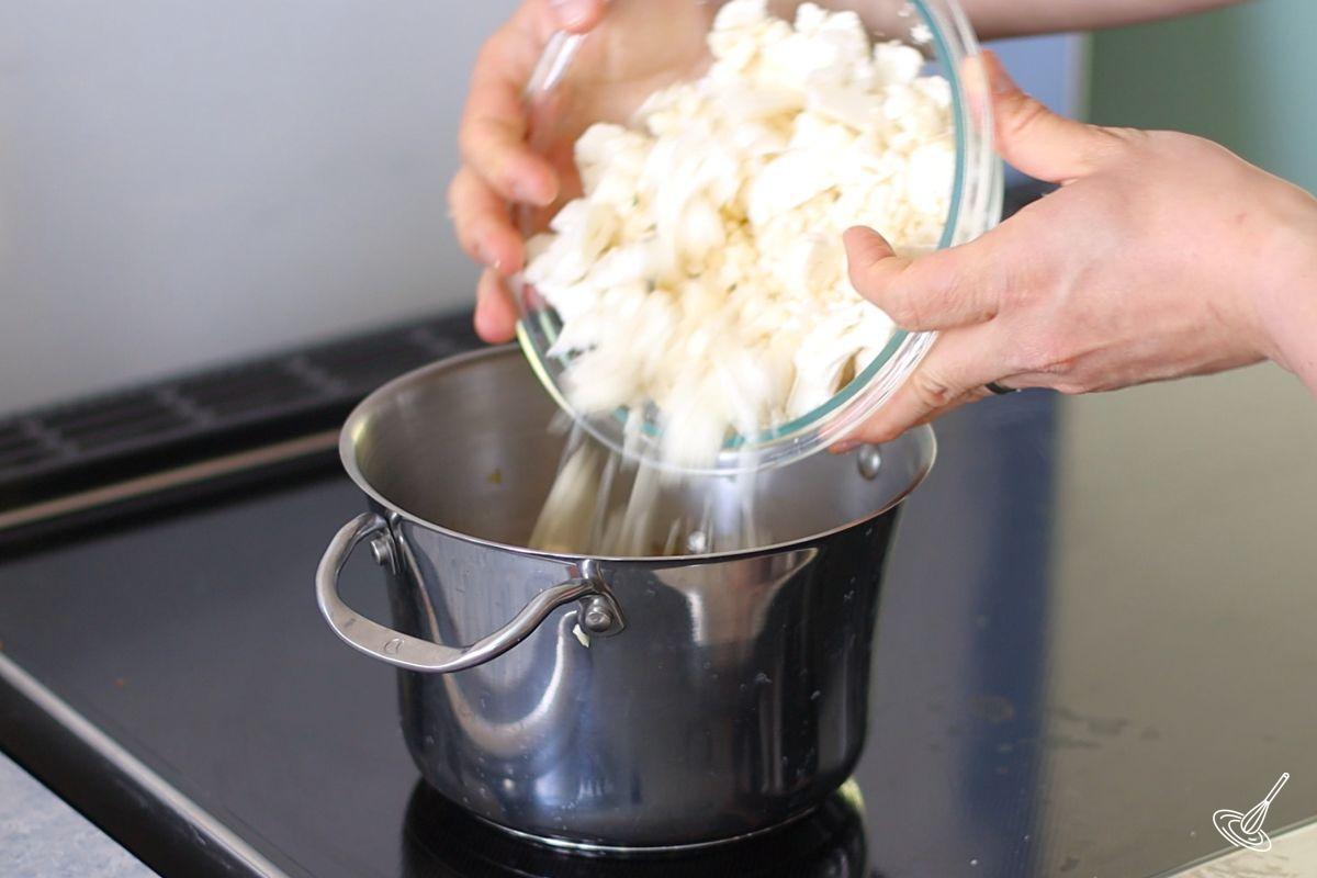 Someone adding chopped cauliflower to a soup pot. 