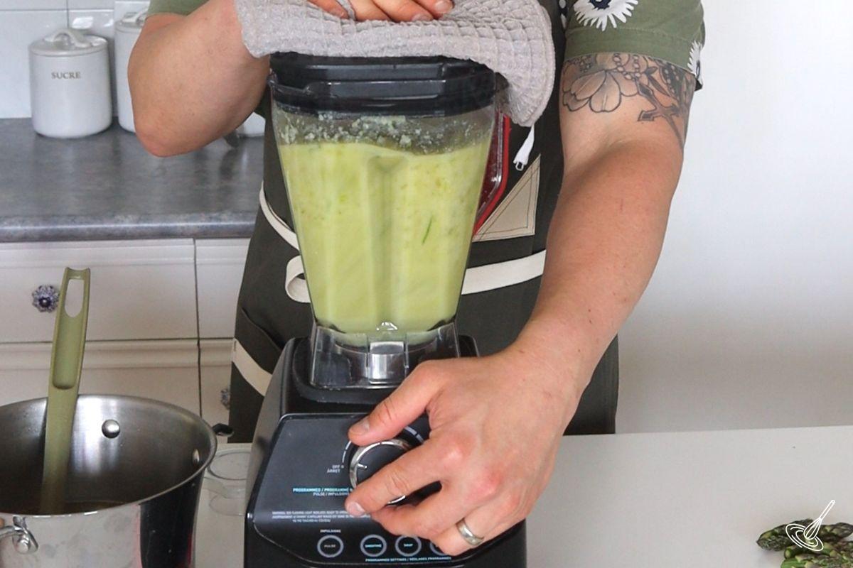 Someone using a high power blender to blend cauliflower asparagus soup. 