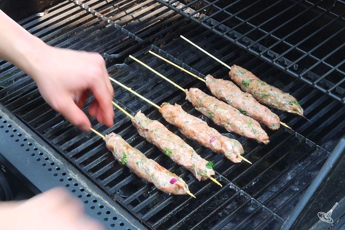 Someone cooking turkey kofta skewers on a grill. 