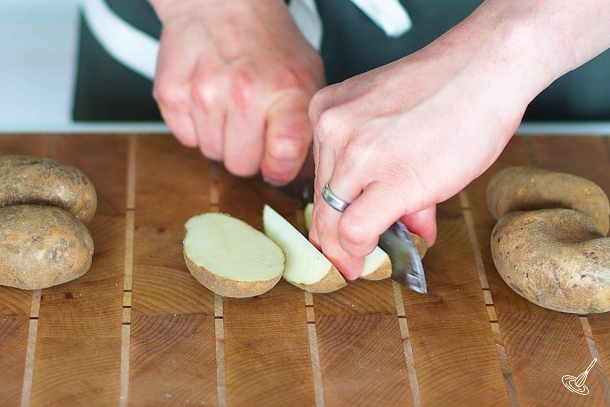 Someone cutting a potato into wedges.