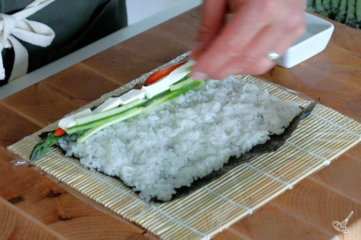 Someone placing filling on the sushi. 