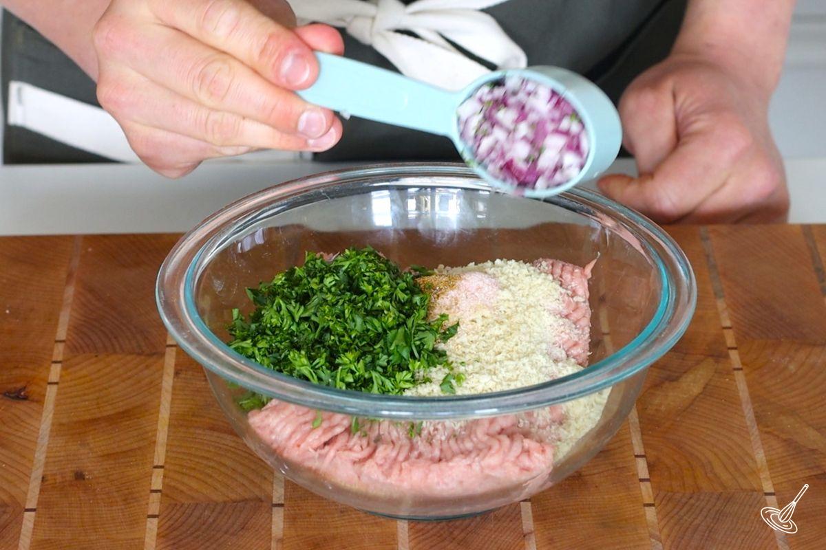 Someone adding chopped red onion to a bowl of ground turkey.