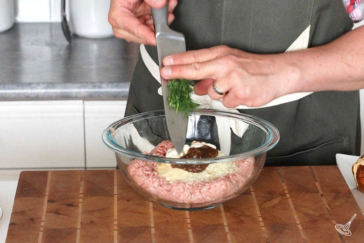 Someone adding chopped dill to a bowl of ground turkey.