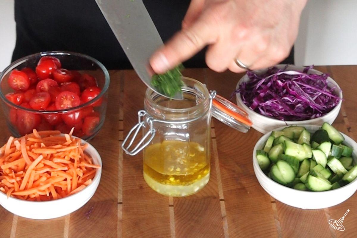 Someone adding chopped dill to a container of lemon salad dressing. 