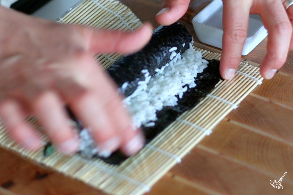 Someone spreading water with their finger to seal the sushi roll.