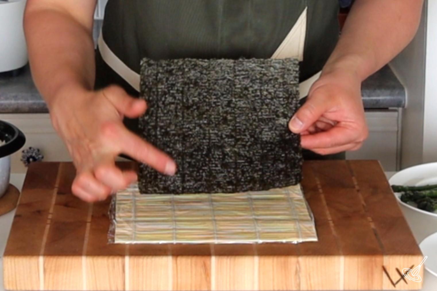 Someone placing a sheet of nori on a sushi mat.