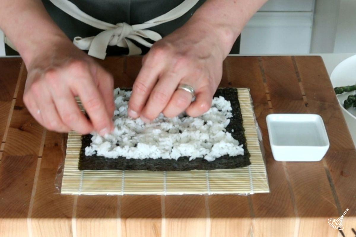 Someone spreading sushi rice on a sheet of nori. 