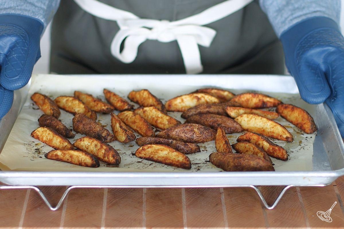 Someone placing a tray of roasted potato wedges on a cooling rack. 