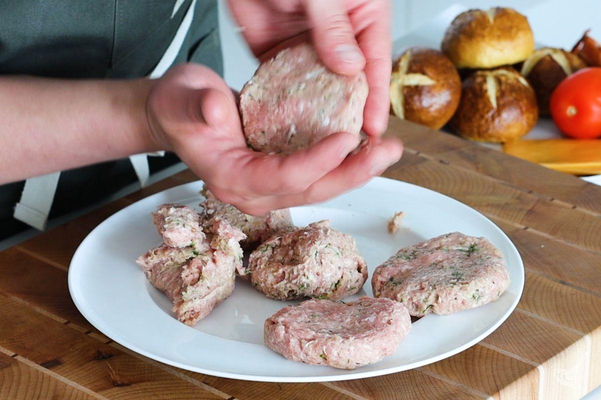Someone using their hands to shape turkey burger sliders. 