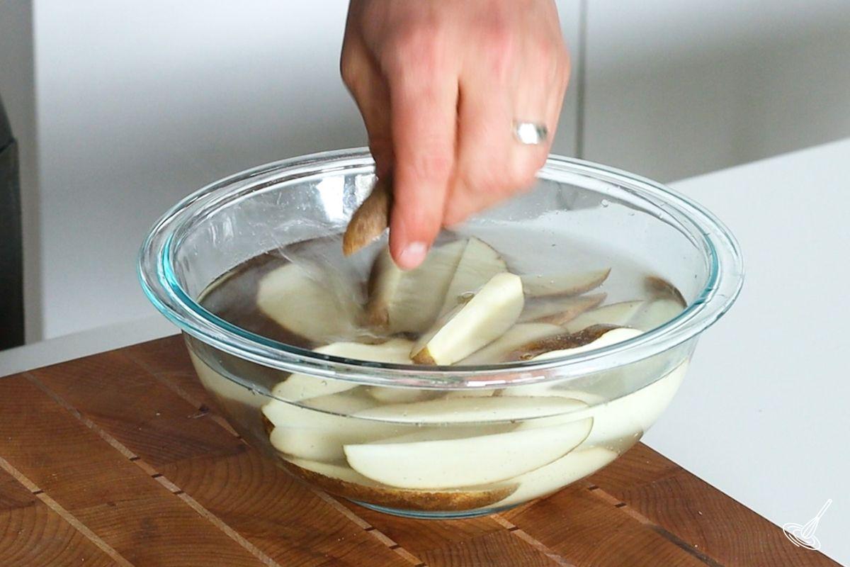 Someone placing potato wedges in a bowl of water.